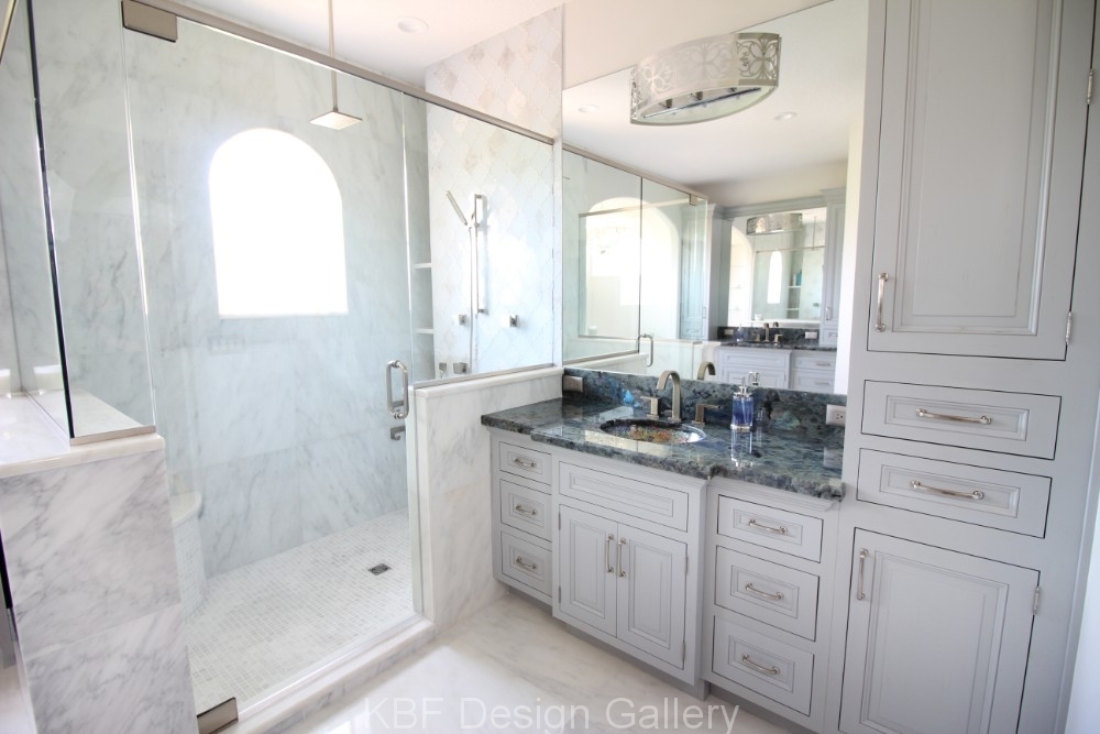 Remodeled marble master bathroom: frameless glass shower with an arched marble-clad window, pale gray inset vanity cabinetry, and a deep blue granite counter