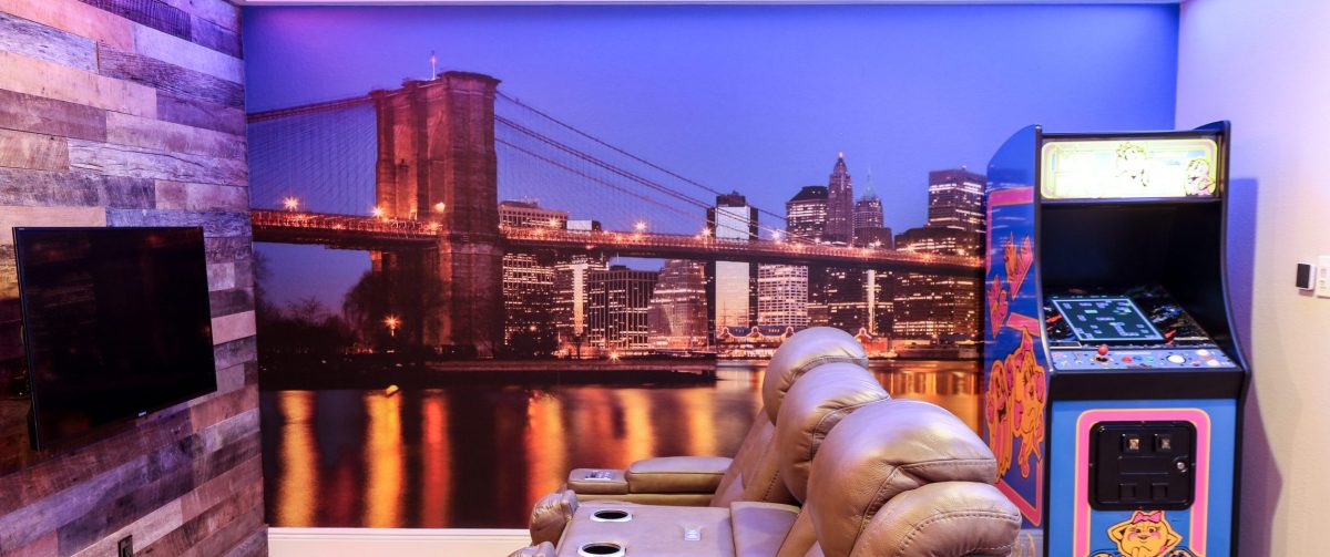 The game end of the room: a floor-to-ceiling Brooklyn Bridge skyline mural behind leather recliners with an arcade cabinet at the wall