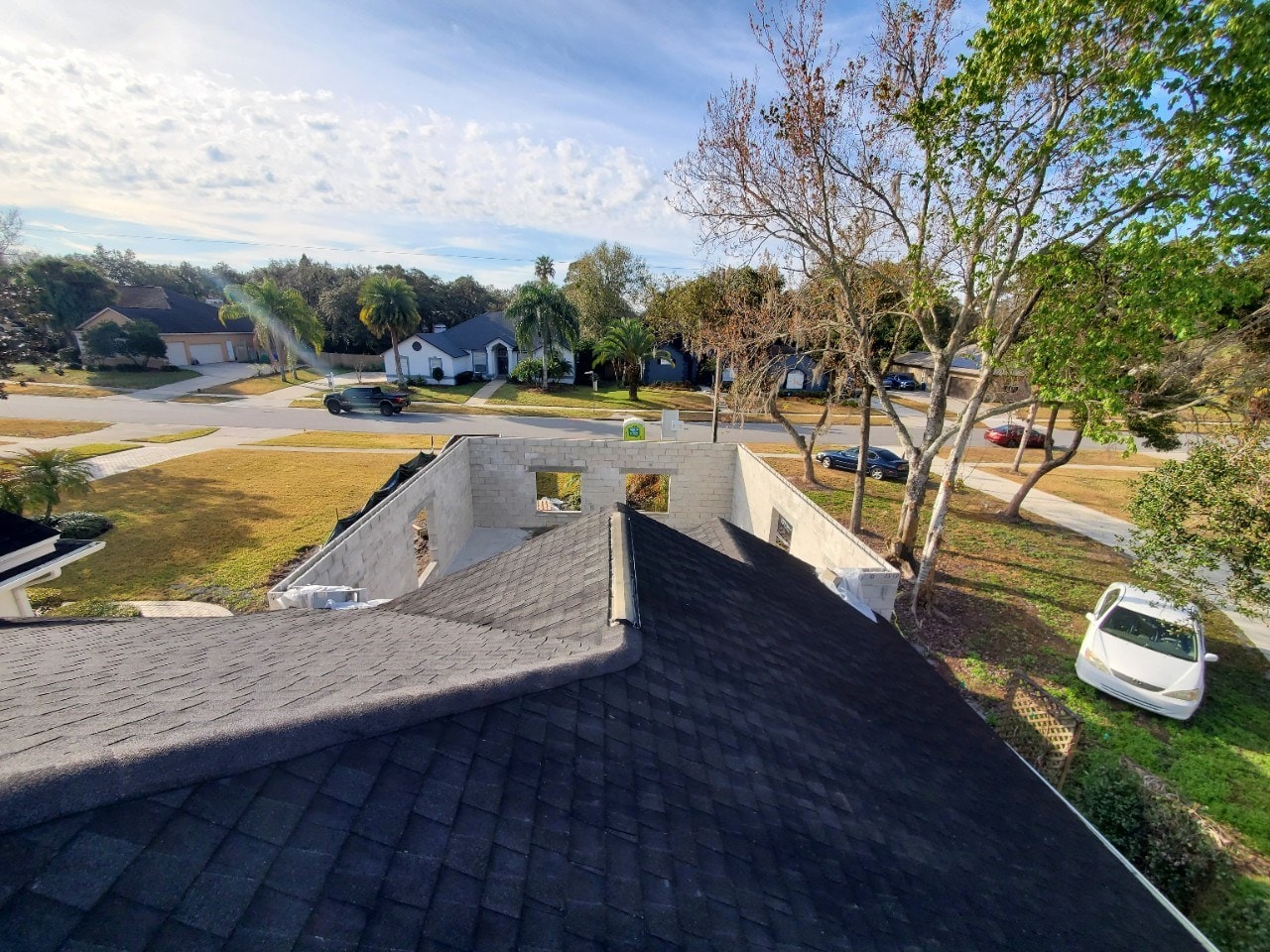 Masonry block walls of a new home addition photographed from the existing shingle roof, with the street, sidewalk and neighboring homes just beyond the new walls