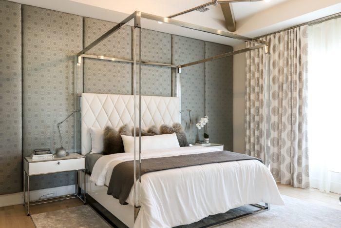 Primary bedroom of the same Orlando residence &mdash; a chrome four-poster canopy bed with a diamond-quilted headboard against upholstered geometric wall panels, white-and-chrome nightstands and patterned drapes