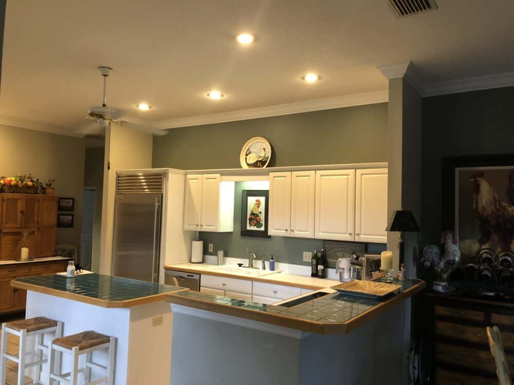 The same Maitland kitchen before its remodel &mdash; white 1980s cabinetry with teal tile counters and a two-level peninsula bar