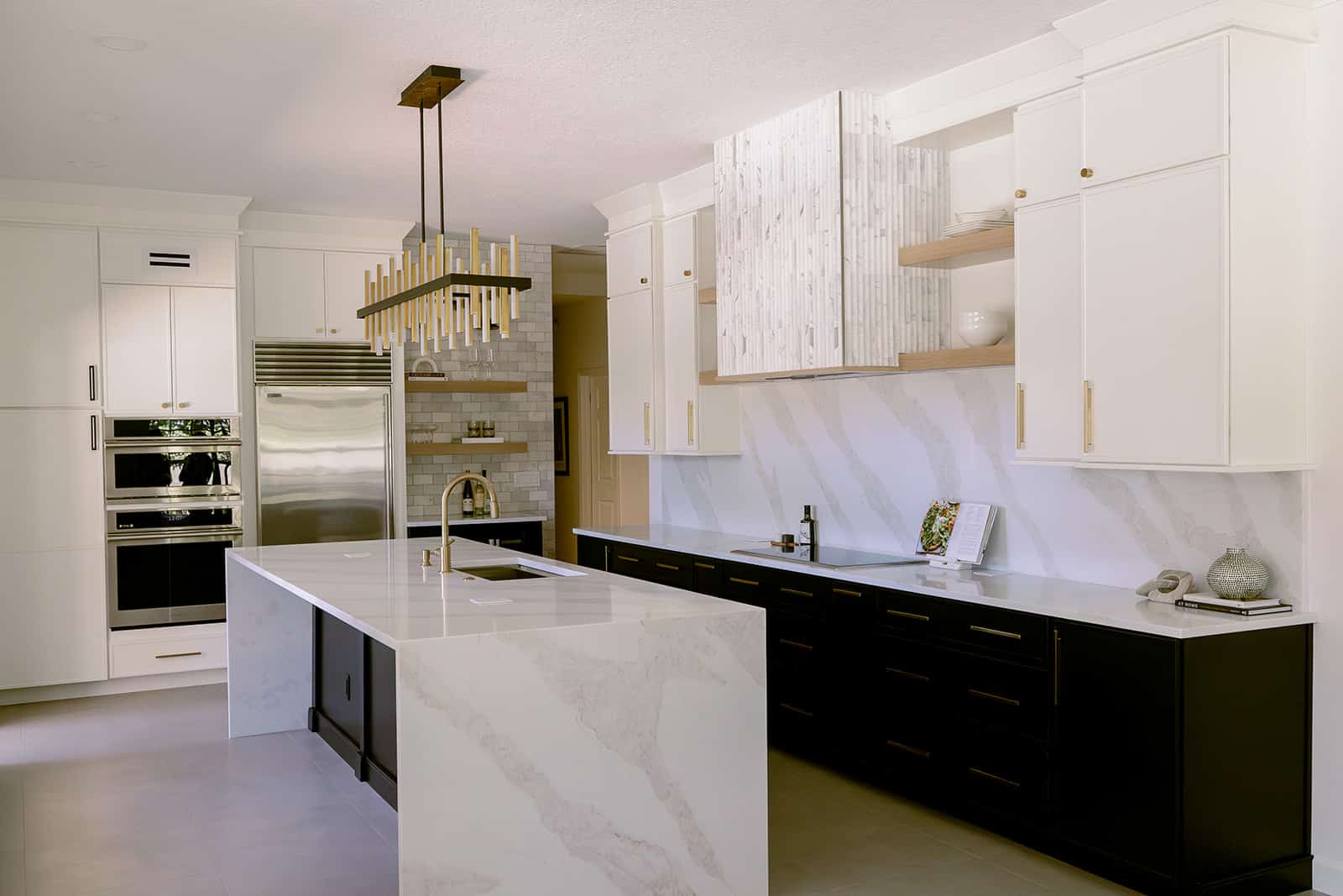 Two-tone kitchen with a fluted marble hood surround, waterfall-edge quartz island and linear brass chandelier &mdash; Maitland kitchen remodel by KBF