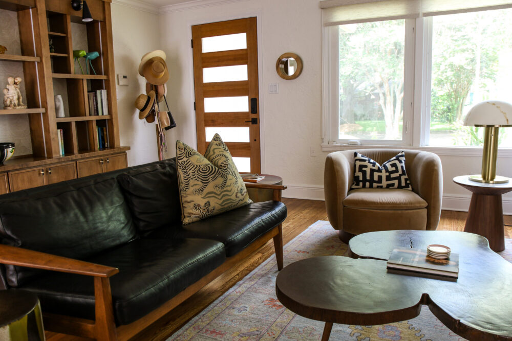 Mid-century modern living room design in Orlando &mdash; black leather sofa, wood built-ins, and sculptural wood coffee tables