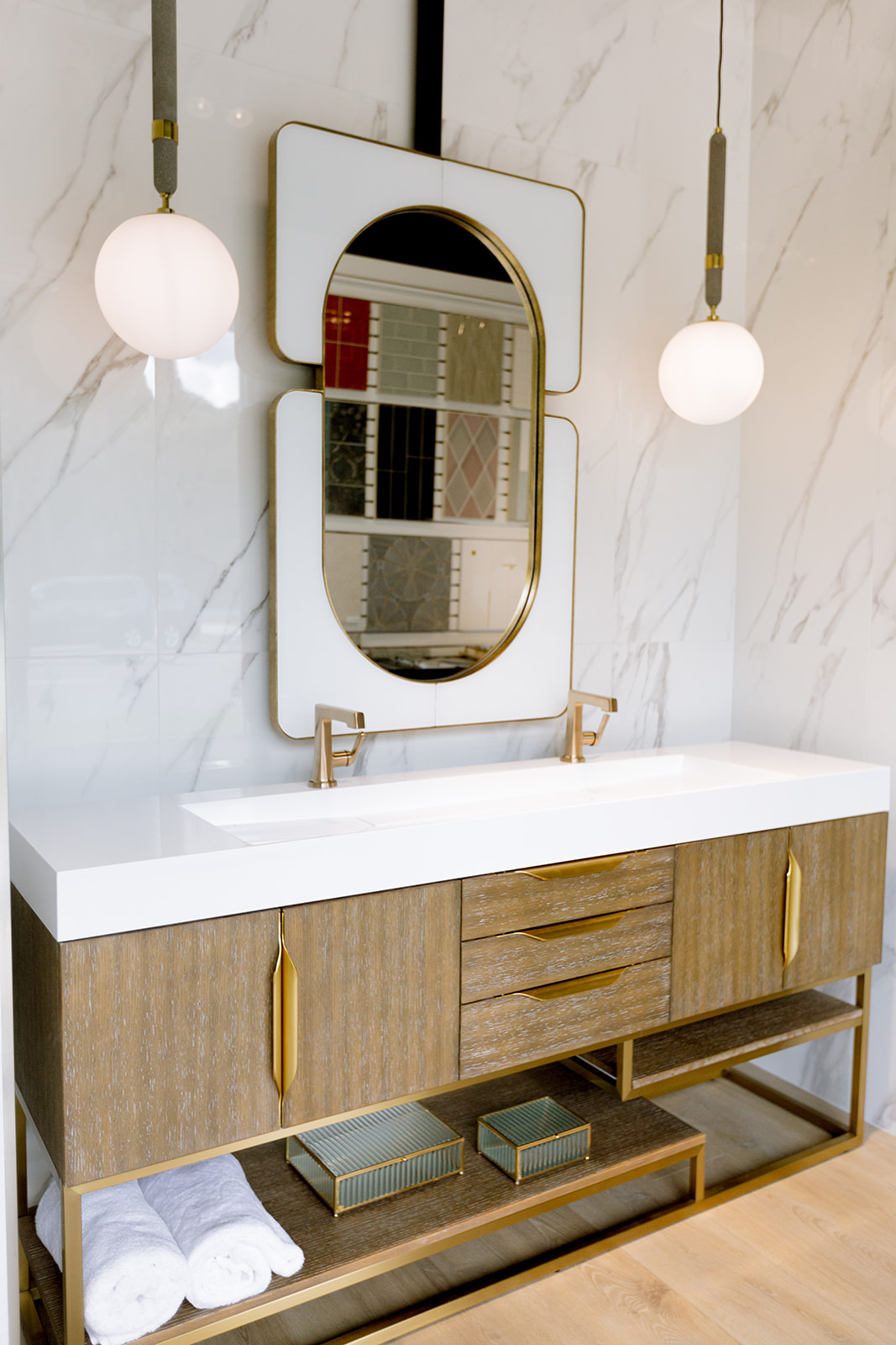 A full-scale bath display inside the KBF Design Gallery showroom &mdash; floating vanity, brass fixtures, and the tile library reflected in the mirror
