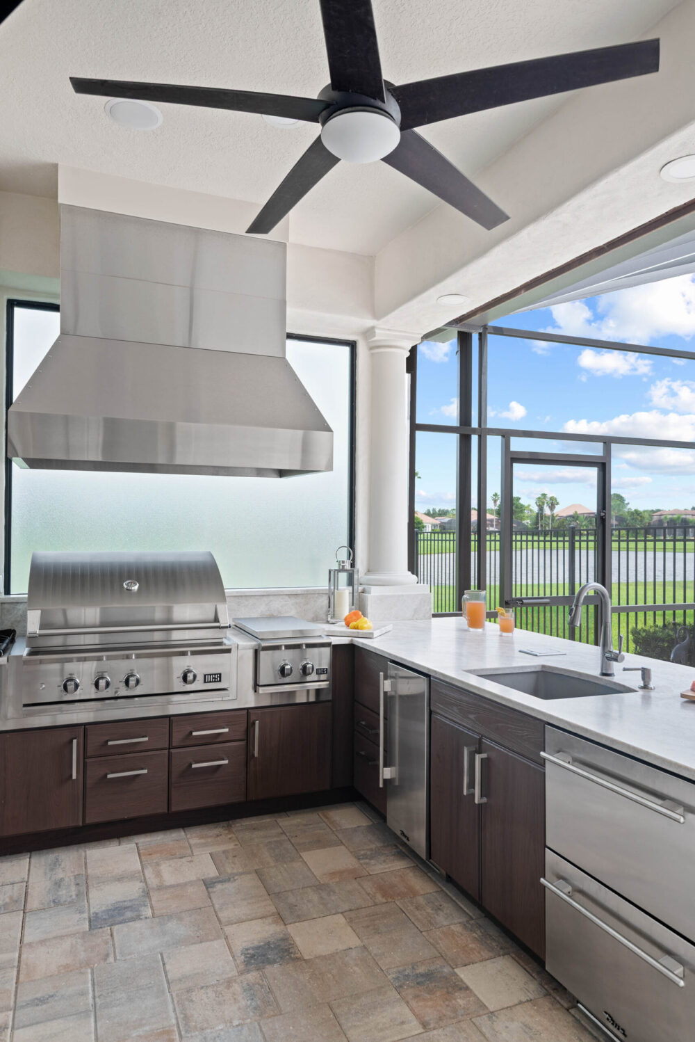 Windermere summer kitchen remodel &mdash; stainless grill, side burners and refrigeration under a steel hood, with water beyond the screen