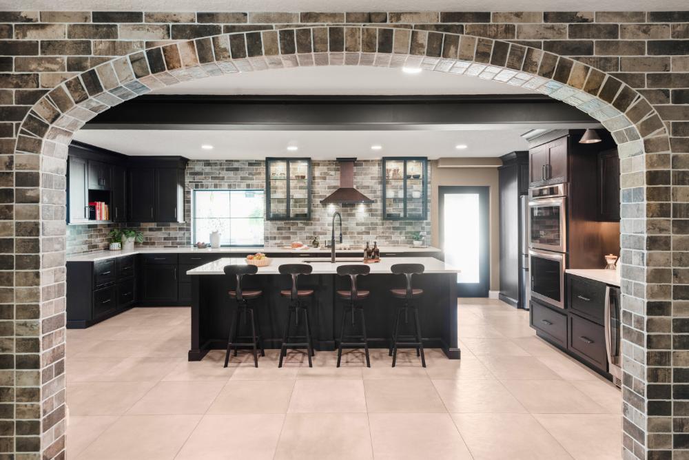 Lake Mary kitchen remodel &mdash; dark oak cabinetry and a white quartz island against a brick-look feature wall, framed by a brick archway with an exposed dark beam overhead