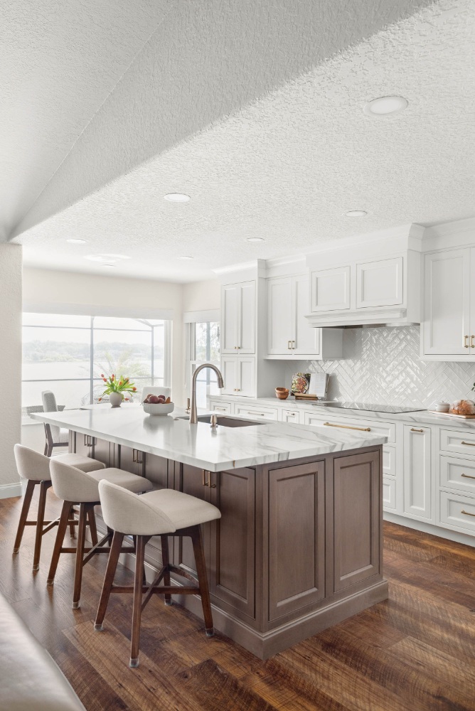 Remodeled lakefront kitchen with a stained-wood island, white perimeter cabinetry, glossy herringbone backsplash, and a large window with a lake view