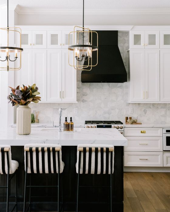 White shaker kitchen with black range hood, gold pendant lights, and marble backsplash