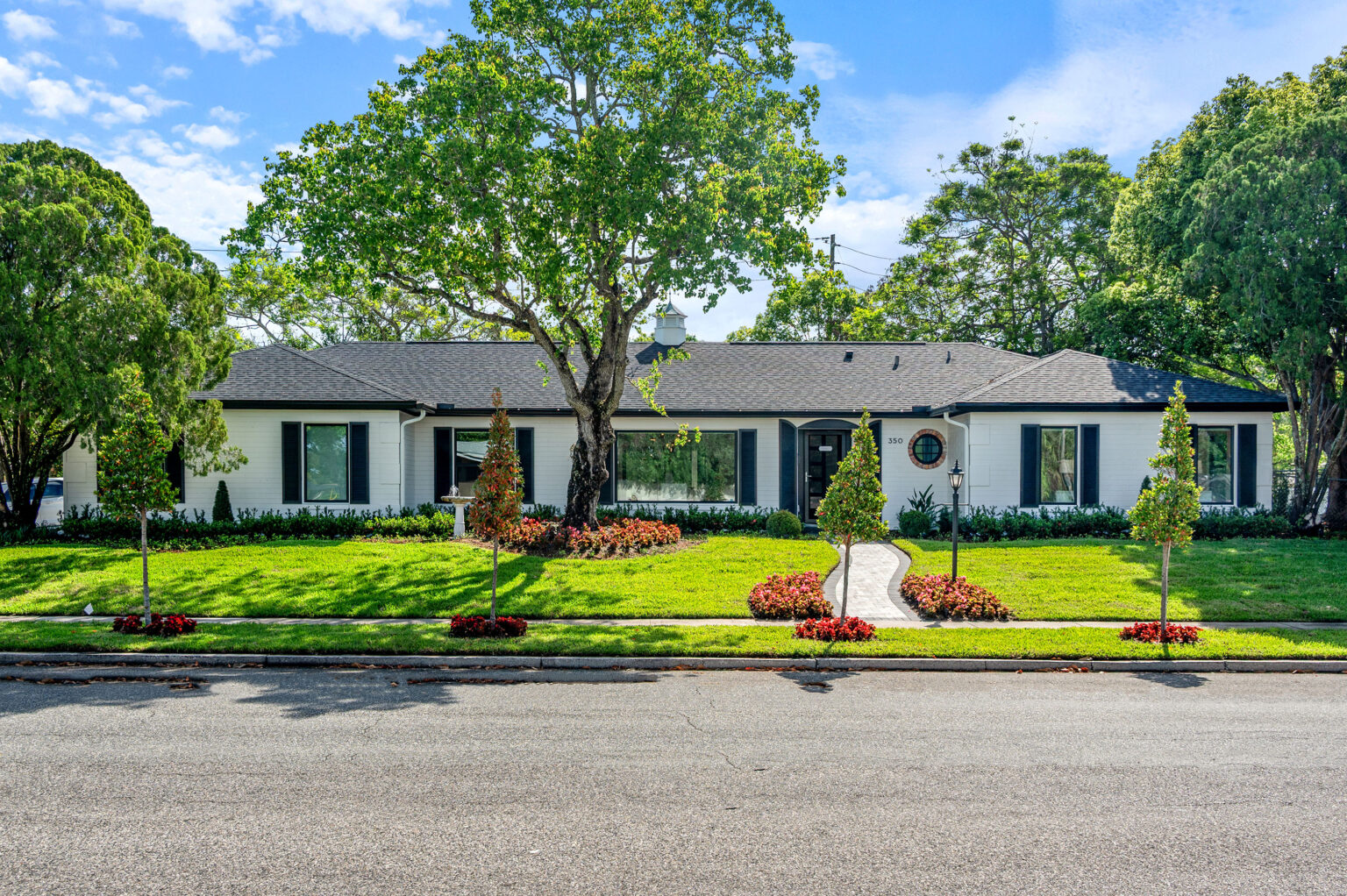 The front of the renovated Winter Park home from the street: a single-story white house with black windows and shutters, new landscaping and mature oaks