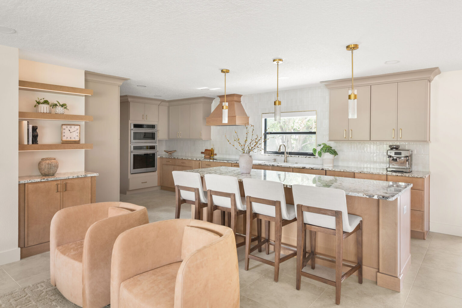 The remodeled kitchen from the family room: a long white oak island with five upholstered stools, brass pendants, pale cabinetry and the sink window straight ahead