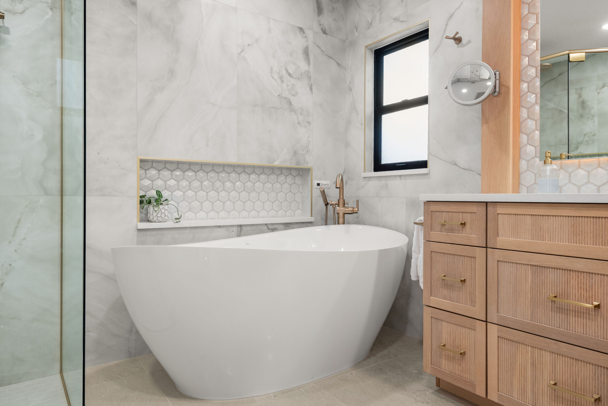 Winter Park whole-home renovation — close detail of the tub, bronze filler, and hexagon-tile niche in raking light