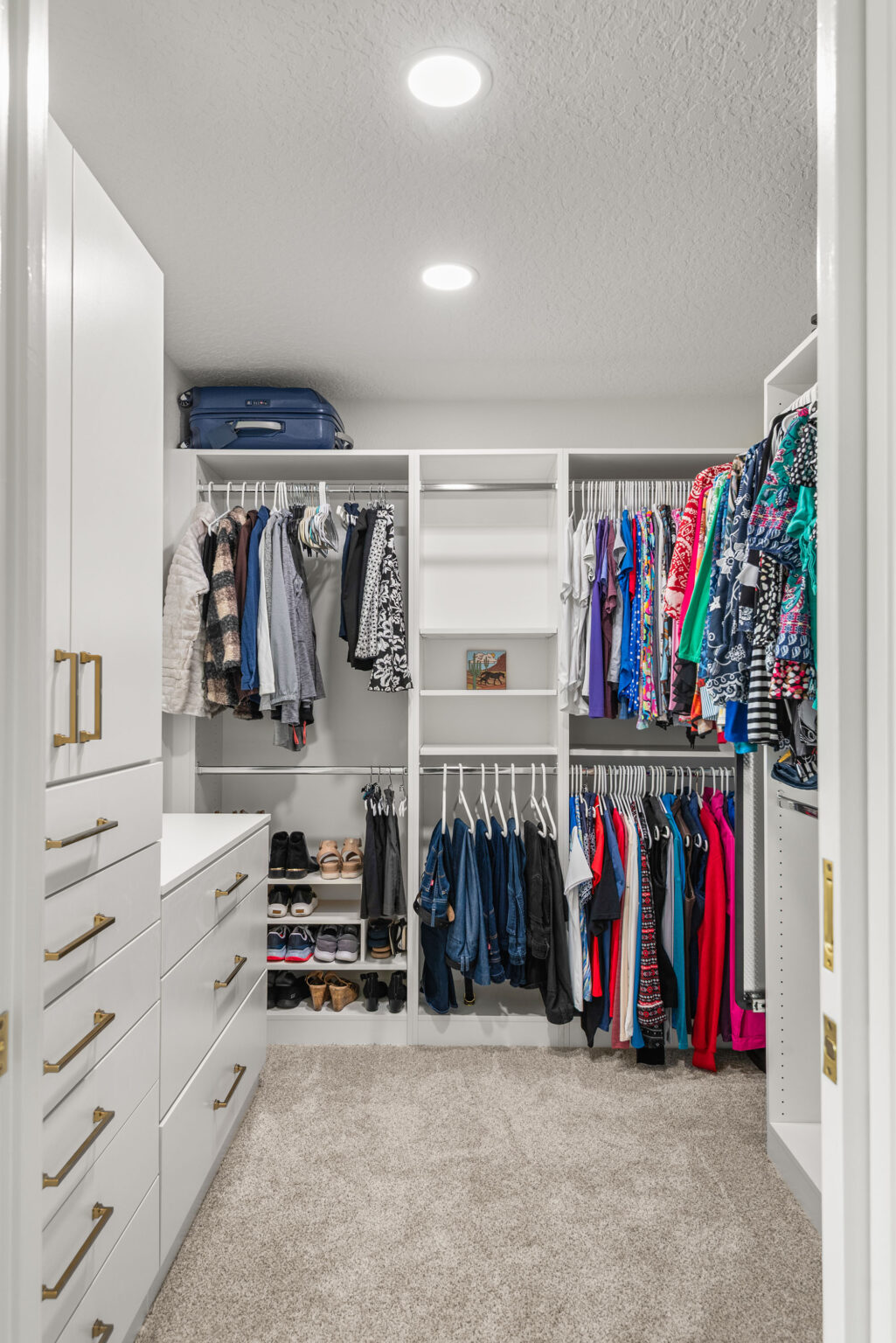 The new walk-in closet built where the original primary bathroom stood, with white built-in drawers, hanging rails and open shelving