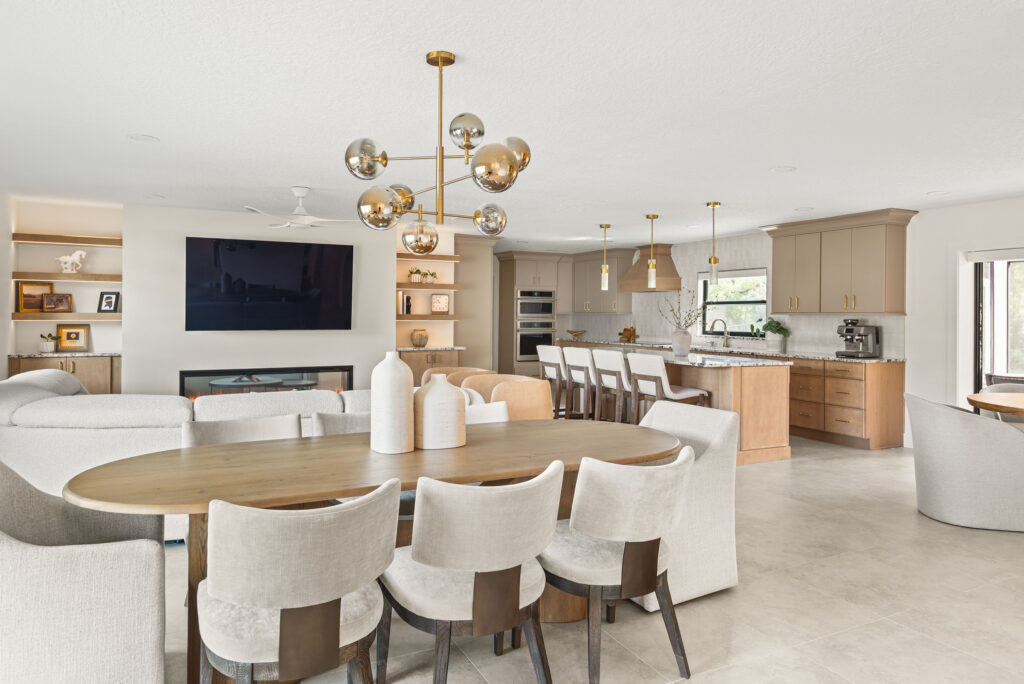 A completed KBF whole-home remodel — dining, living and kitchen opened to one another, a brass globe chandelier over the oval table and a linear fireplace in the built-ins