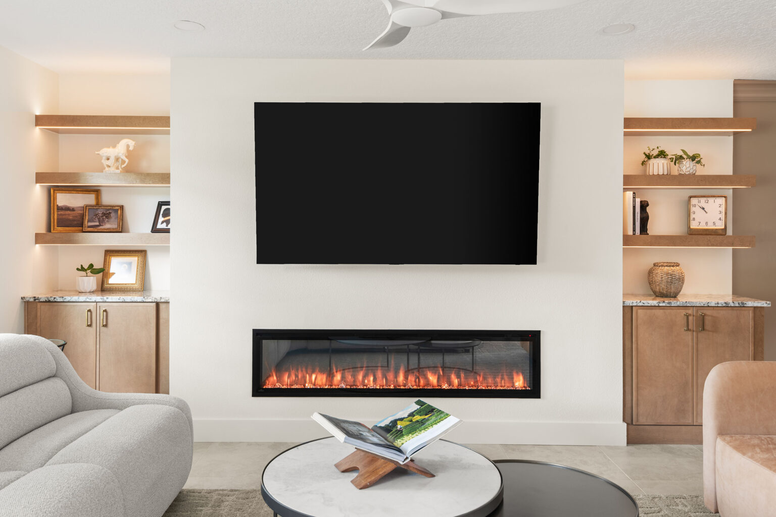 The living room fireplace wall after the remodel: a linear fireplace beneath a wall-mounted television, flanked by lit white oak built-in shelving