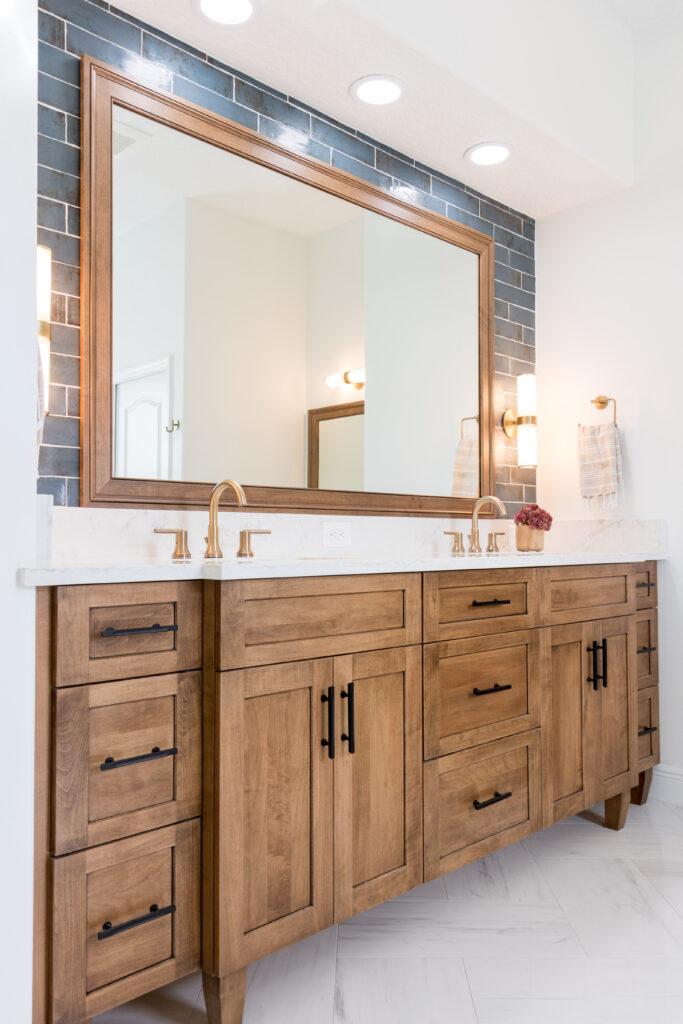 Wood double vanity with a blue subway-tile accent wall and brass faucets in a Baldwin Park bathroom remodel by KBF Design Gallery