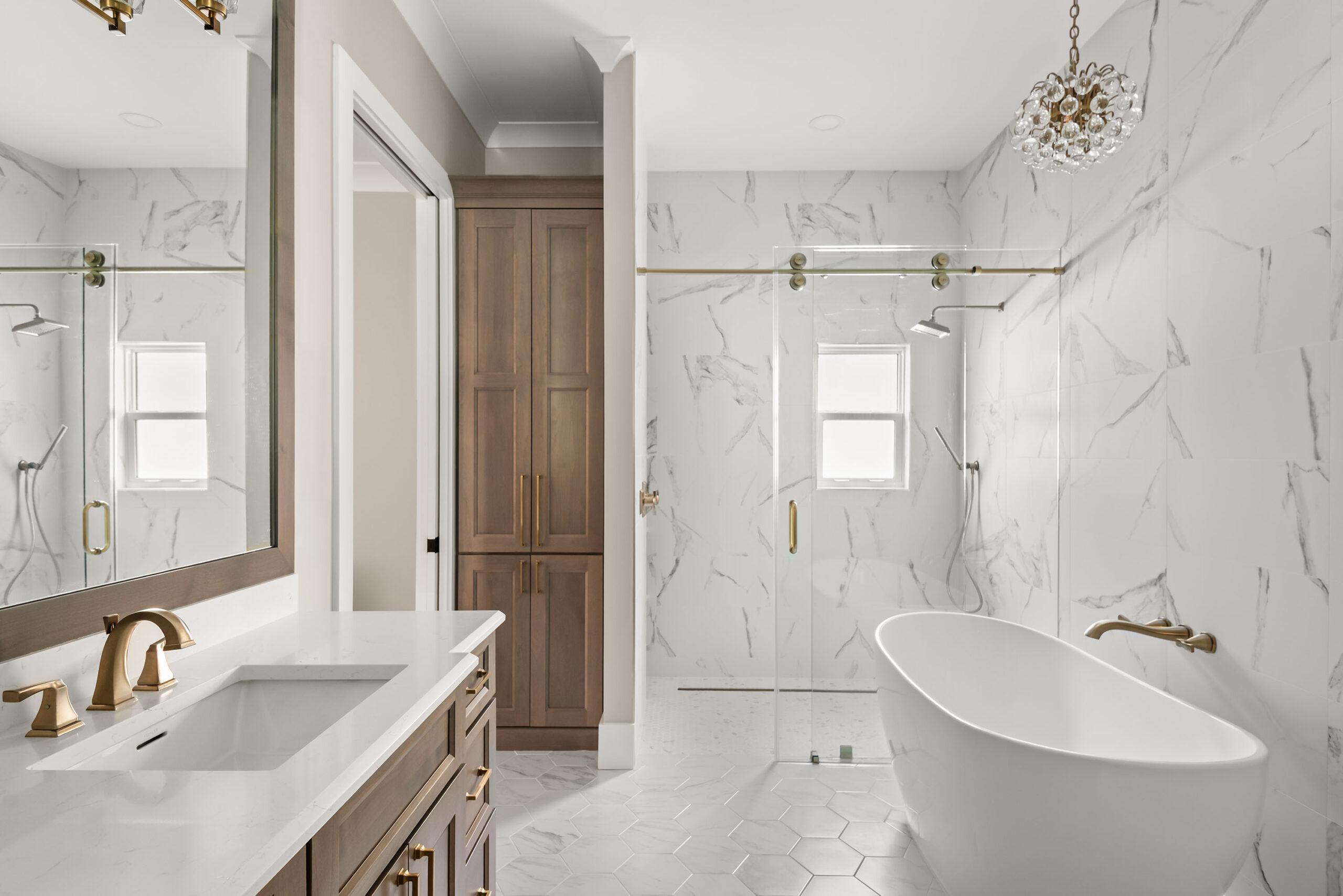 Primary suite bathroom with a freestanding tub, glass walk-in shower, and wood vanity with brass fixtures in a Baldwin Park home remodeled by KBF Design Gallery