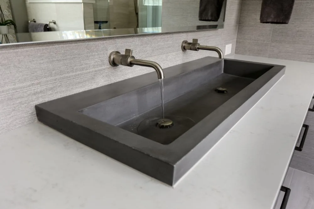 Detail from the concrete master bath &mdash; the integrated concrete trough sink with two wall-mounted nickel faucets, water running