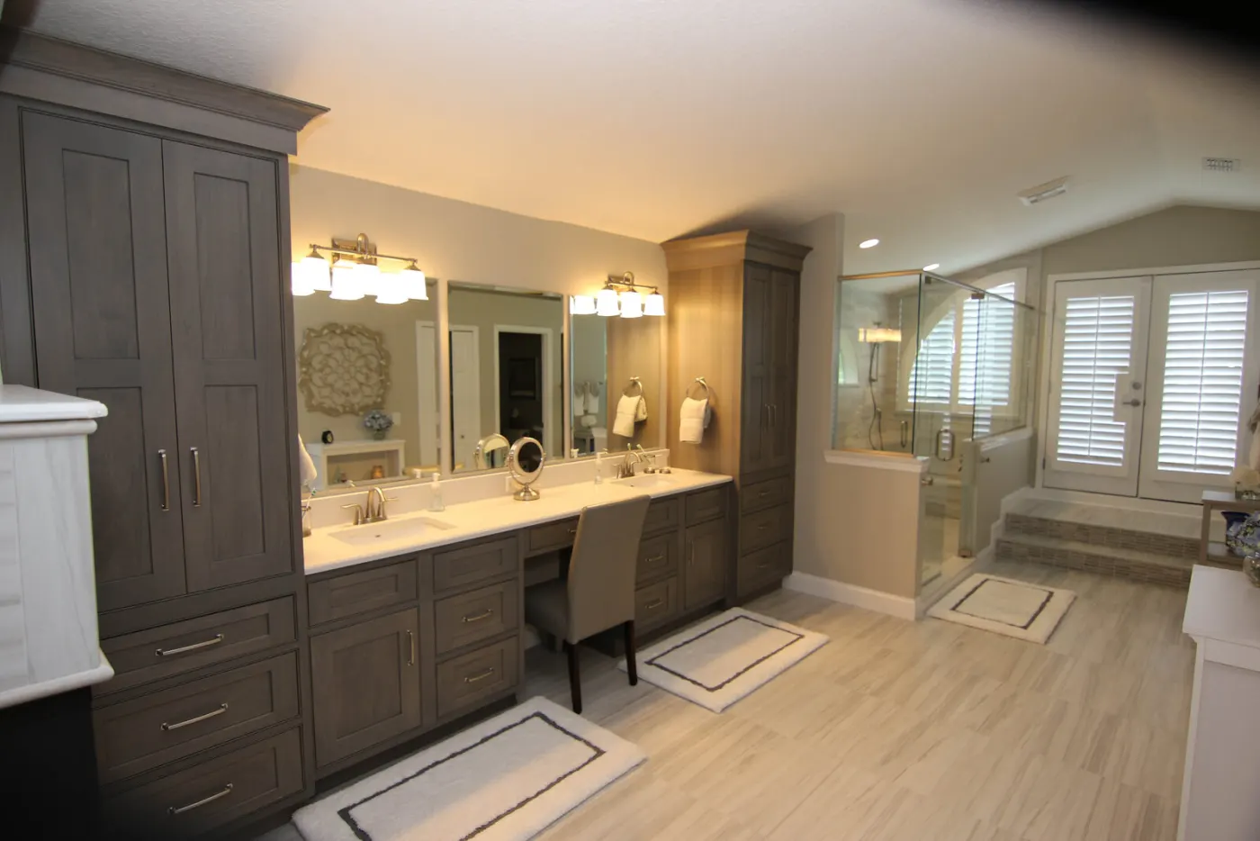 The master bathroom after completion — driftwood-gray double vanity, makeup desk and glass shower