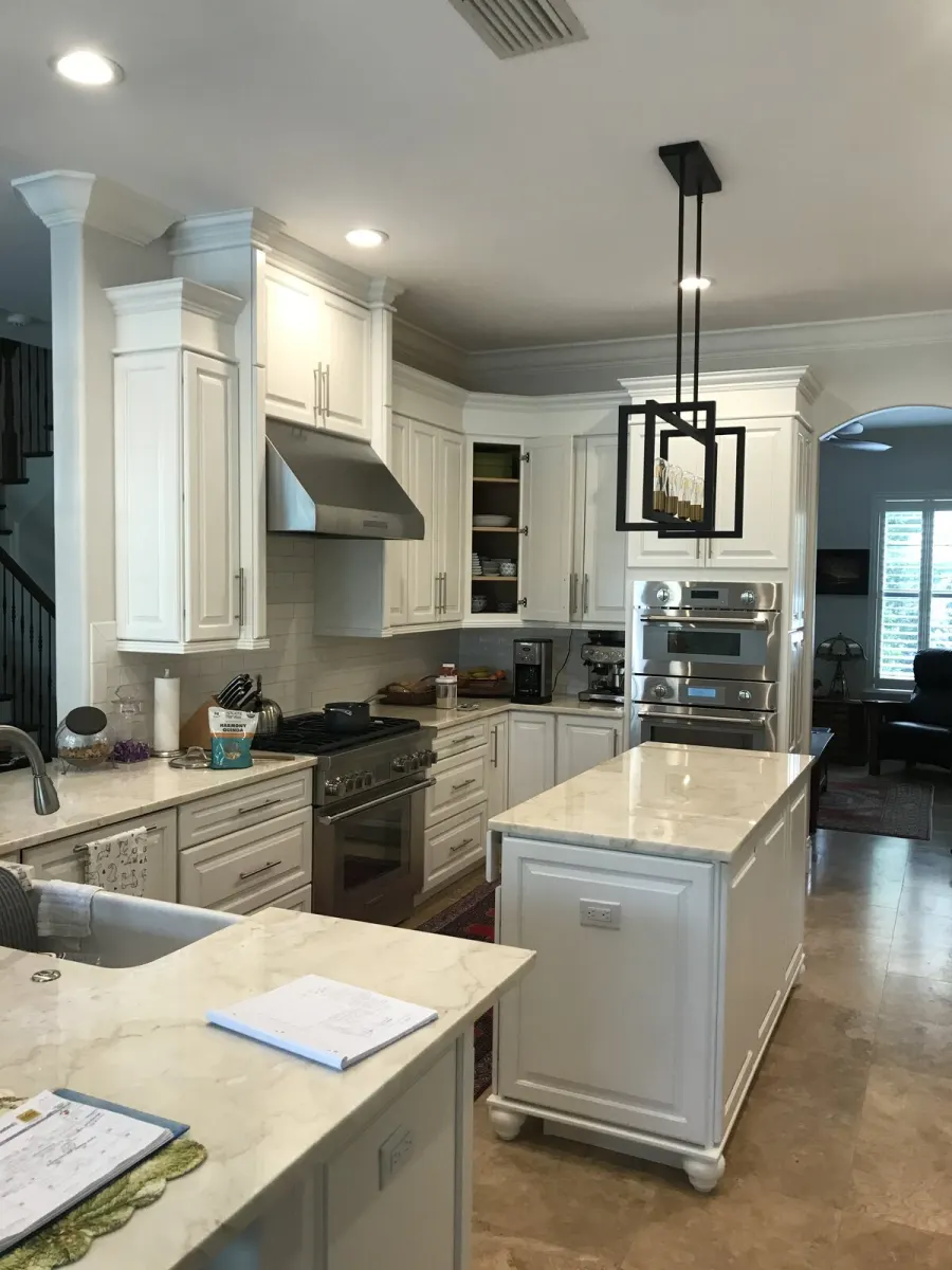 The kitchen &mdash; white cabinetry, marble island, stainless hood and double ovens