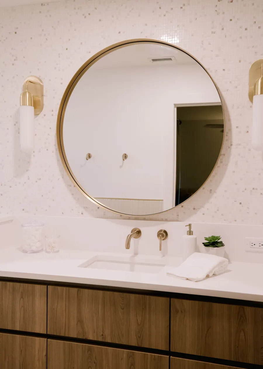The bathroom vanity — round brass mirror and wall-mounted faucet