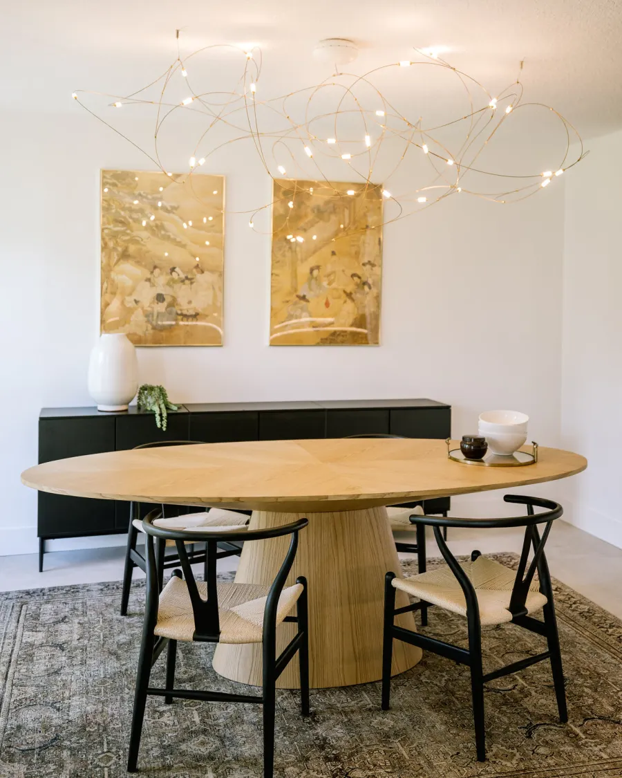 A completed KBF dining room — a round oak table with wishbone chairs under a sculptural chandelier