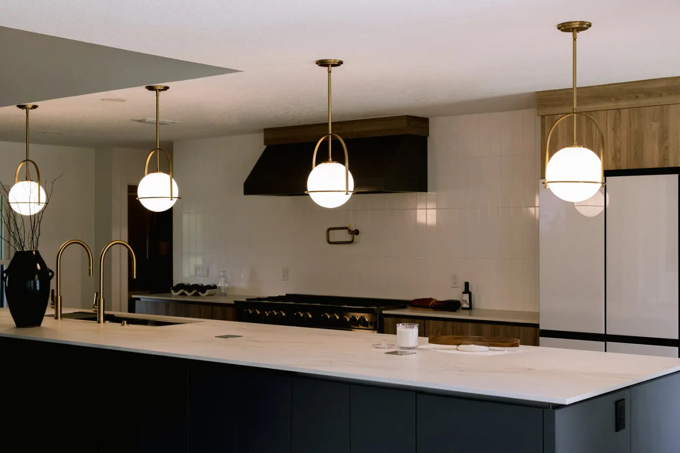 A completed KBF kitchen — a slab-front island under brass pendants, with a professional range and hood on the wall beyond