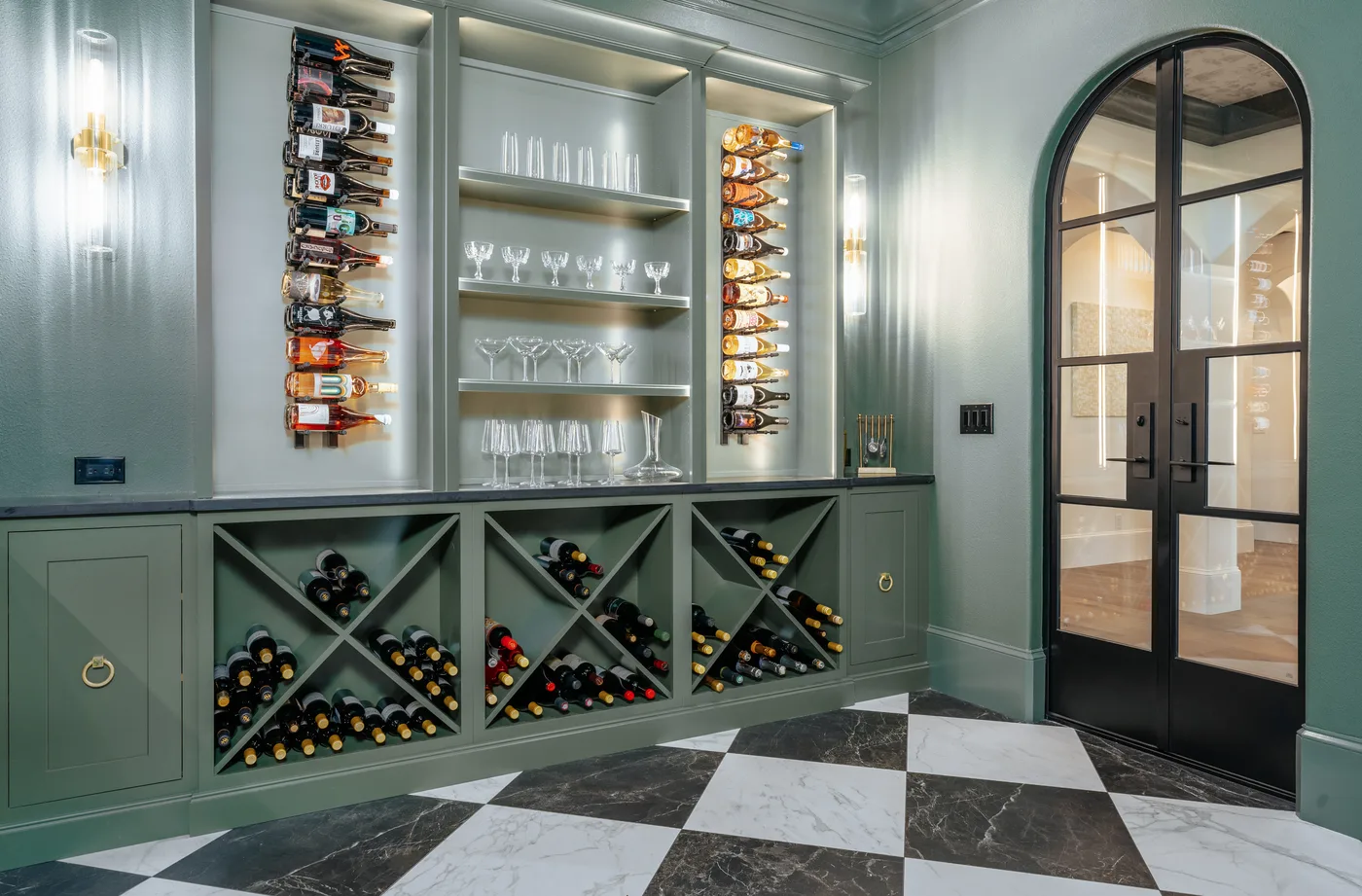 The wine and entertaining room &mdash; sage-green cabinetry, a black-and-white checkerboard marble floor and X-lattice bottle storage behind an arched steel-and-glass door