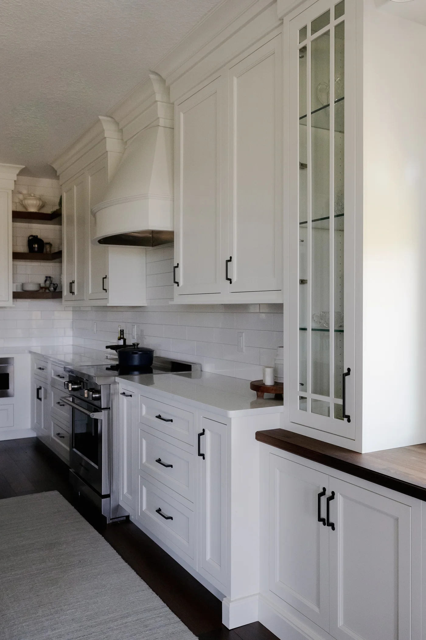 Detail from the two-tone kitchen &mdash; the working run: range, custom arched hood and glass display cabinet over a black-walnut-topped buffet