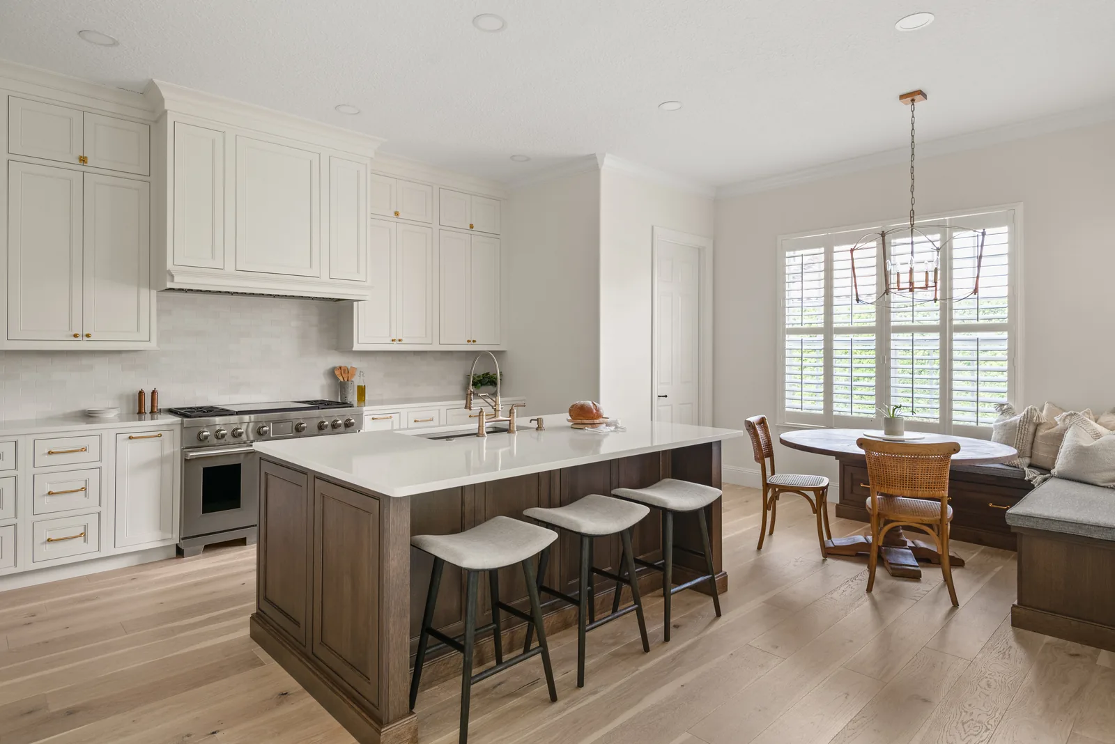 The kitchen opening to the breakfast nook — walnut island with cream stools, range wall beyond, and a built-in window bench