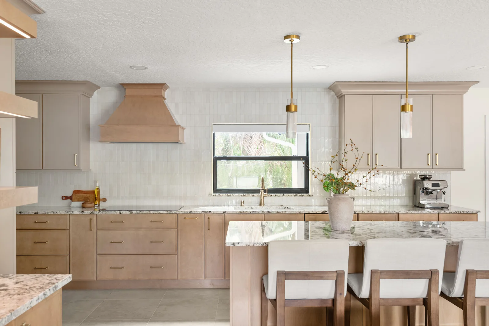 The finished kitchen from the sink-window wall &mdash; painted perimeter cabinetry under dramatically veined stone, a white-oak hood, brass-trimmed pendants and a seated white-oak island