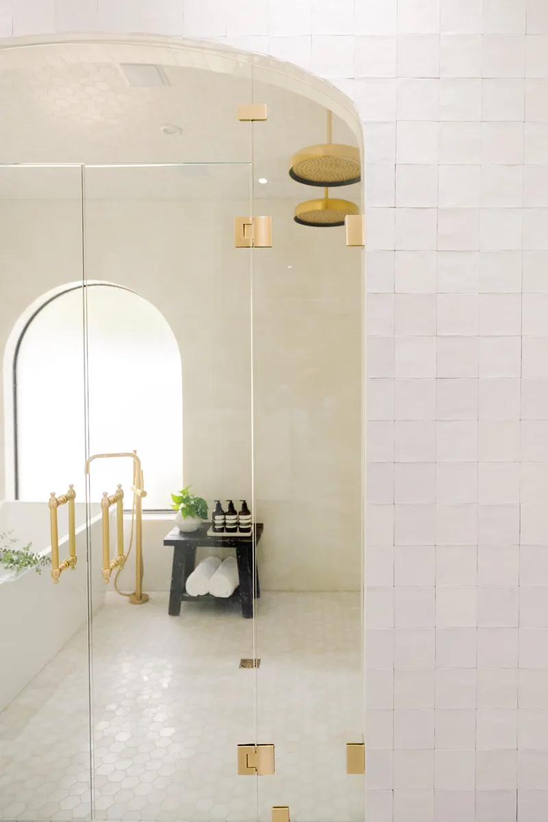 The arched steam-shower enclosure in a Winter Springs primary bath — frameless glass under a tiled arch, twin brass ceiling rain heads against a honed hex mosaic
