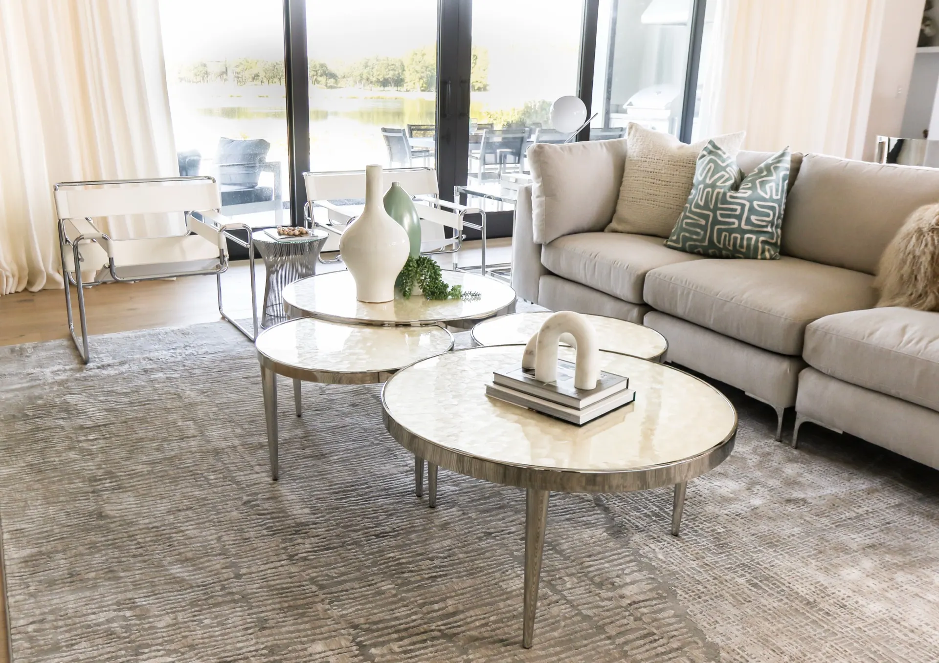 Living room of a whole-residence interior-design project in Orlando &mdash; chrome-and-white-leather lounge chairs, nesting capiz-top cocktail tables, and a linen sectional facing lake-view glass doors