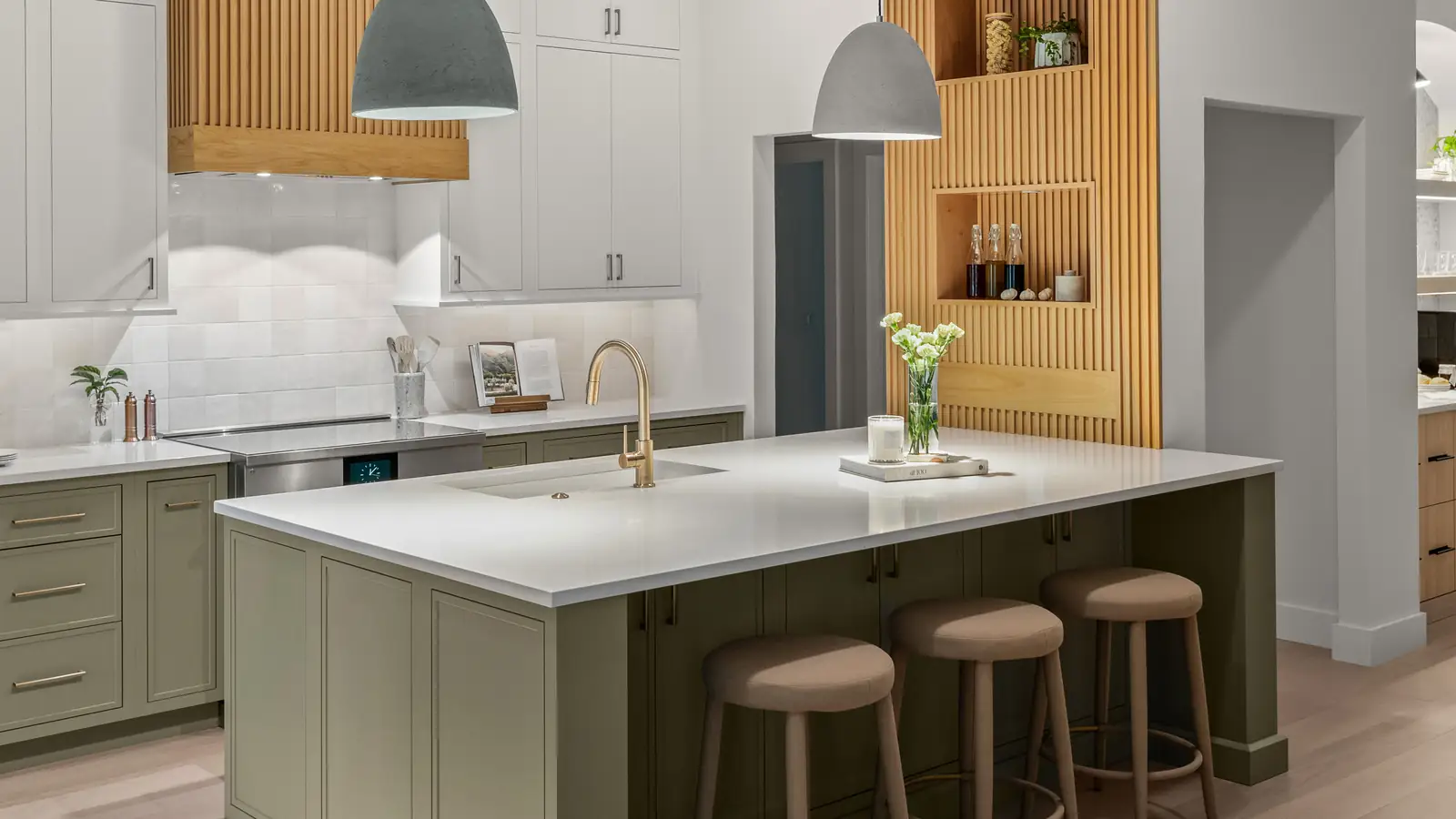 A completed KBF custom kitchen in Celebration, Florida: a sage-green island under white quartz with a brass faucet, white perimeter cabinetry, and a fluted terracotta hood and slat wall under grey dome pendants