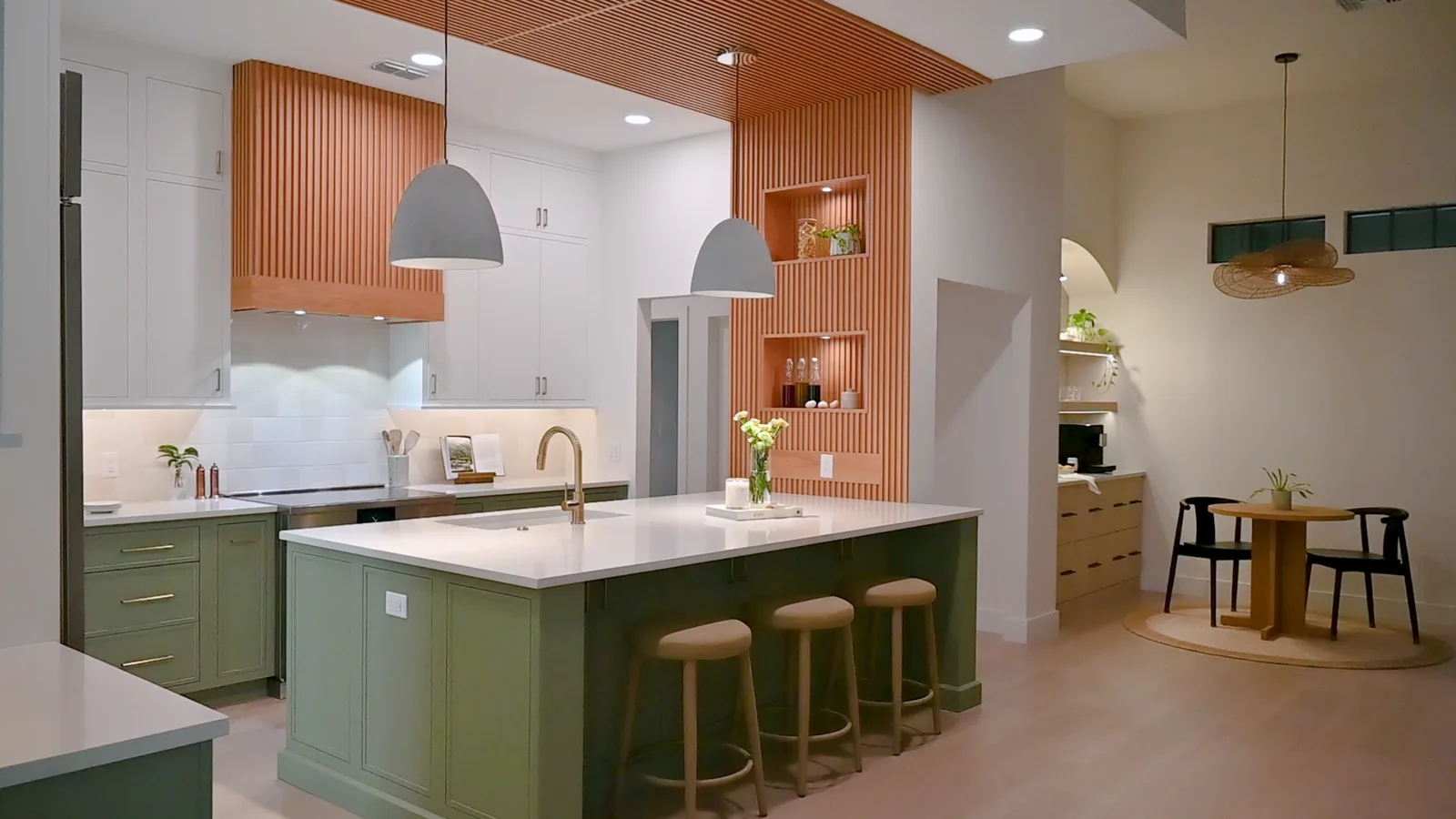 A completed KBF custom kitchen in Celebration, Florida: sage-green island with brass hardware, white perimeter cabinetry and a fluted terracotta hood wall under warm pendant light