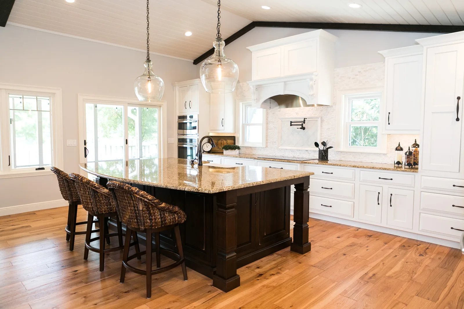 Lake Sybelia whole-home remodel in Maitland &mdash; the kitchen's dark paneled island with turned legs under clear glass pendants, a corbeled custom hood and a shiplap vaulted ceiling