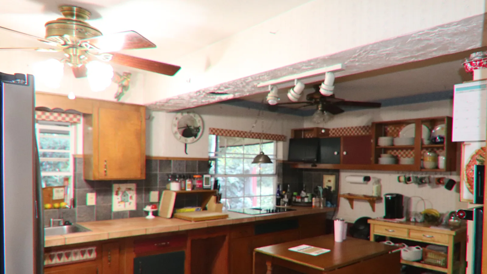 The same Maitland kitchen as found — oak cabinets, tile counters and a terracotta tile floor seen through the doorway of the wall that closed the room off, with a ceiling fan and a small drop-leaf table in the middle