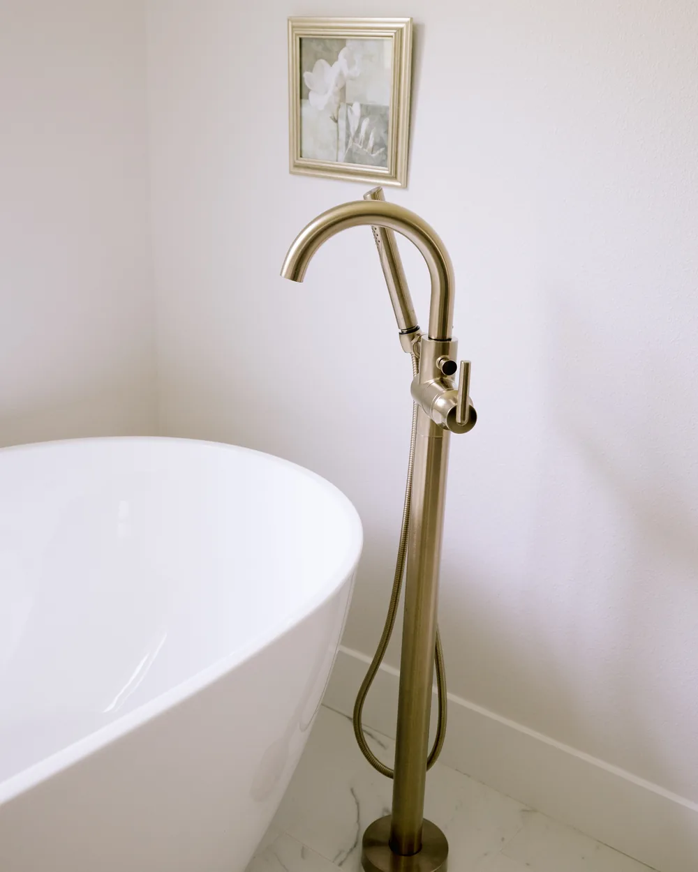 Detail from the Maitland whole-home primary bath — a freestanding soaking tub beside a brass floor-mounted tub filler on marble-look tile