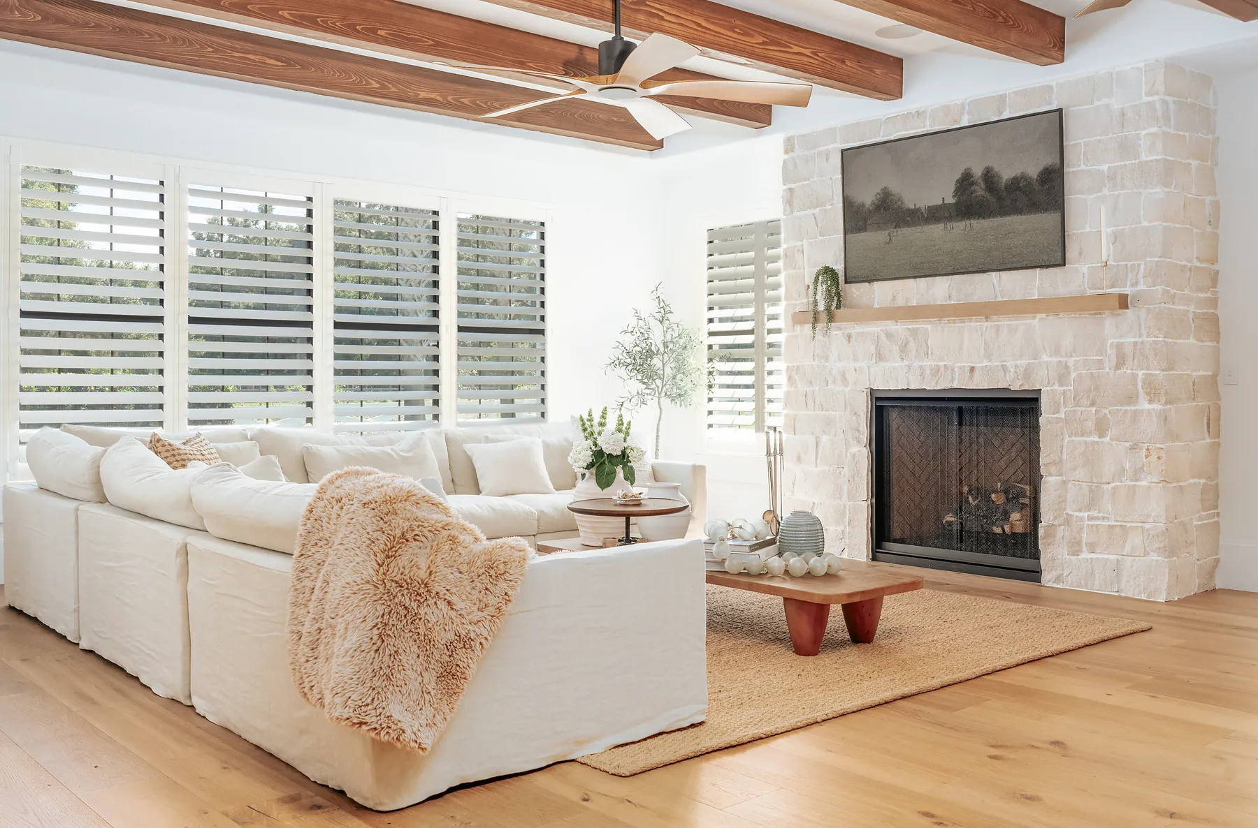A finished KBF living room — beamed ceiling, stone fireplace, wide-plank wood floors and interior shutters, every element specified during the design phase