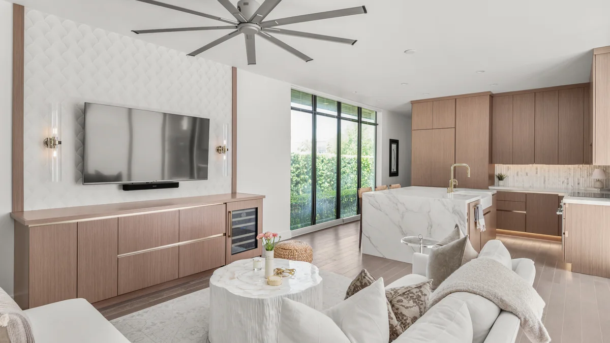 A Studio KBF project in Winter Park: the panelled entertainment wall with its wood-grain storage run on the left and the remodelled kitchen with its marble-veined quartz island on the right, both in one open room