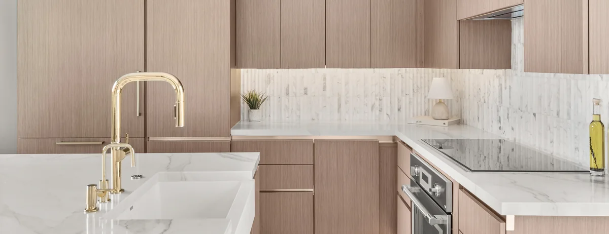 The curated Studio KBF palette on a Winter Park kitchen: wood-grain slab cabinetry, a stacked-mosaic backsplash, a marble-veined quartz counter, warm brass fittings and a flush induction cooktop