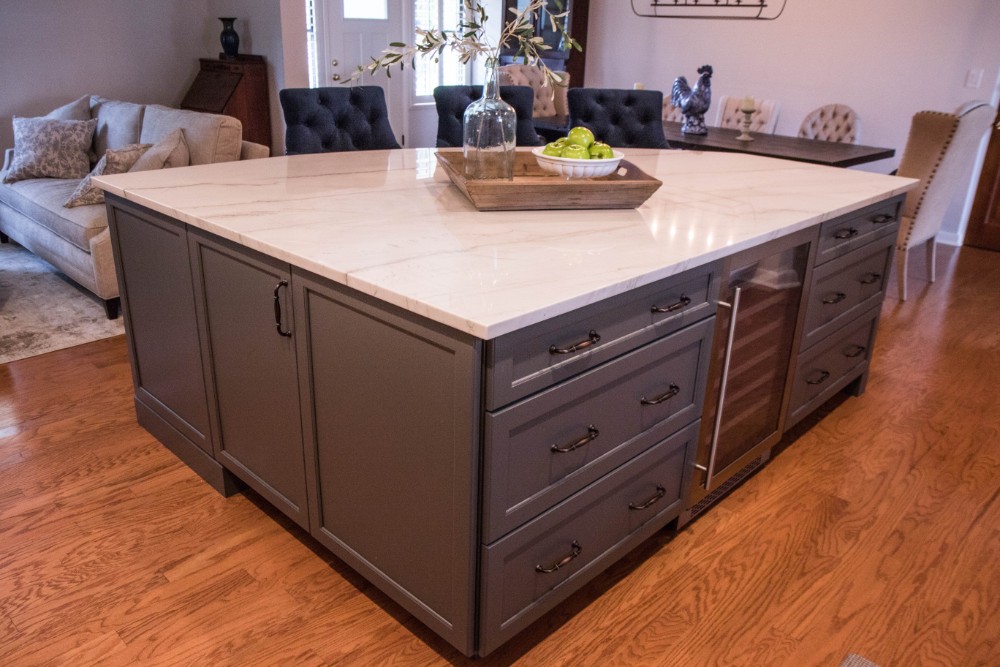 Large gray kitchen island with marble-look quartz top, paneled ends, a built-in beverage refrigerator, and storage drawers