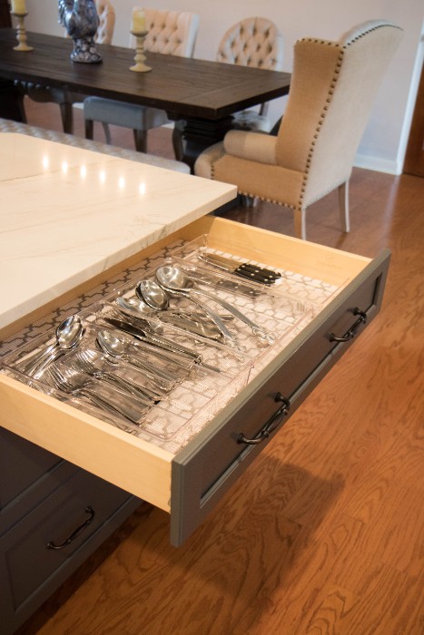 Open island drawer with an organized cutlery insert, dining table in the background
