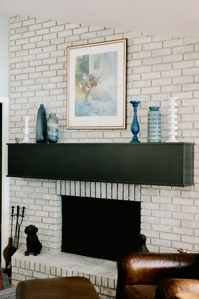 Painted white brick fireplace with a floating black metal mantel in the adjoining family room, from the same published project gallery