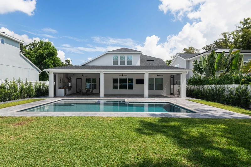 A completed KBF home addition seen across the pool — a full-width covered living space and summer kitchen tied into the original house under a continuous new roofline