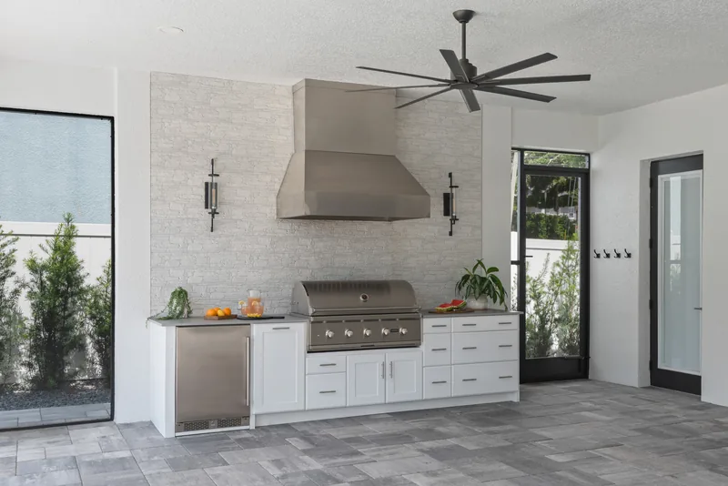 Summer kitchen detail under the addition's ceiling fan &mdash; sconces, stone wall, and outdoor-rated cabinetry