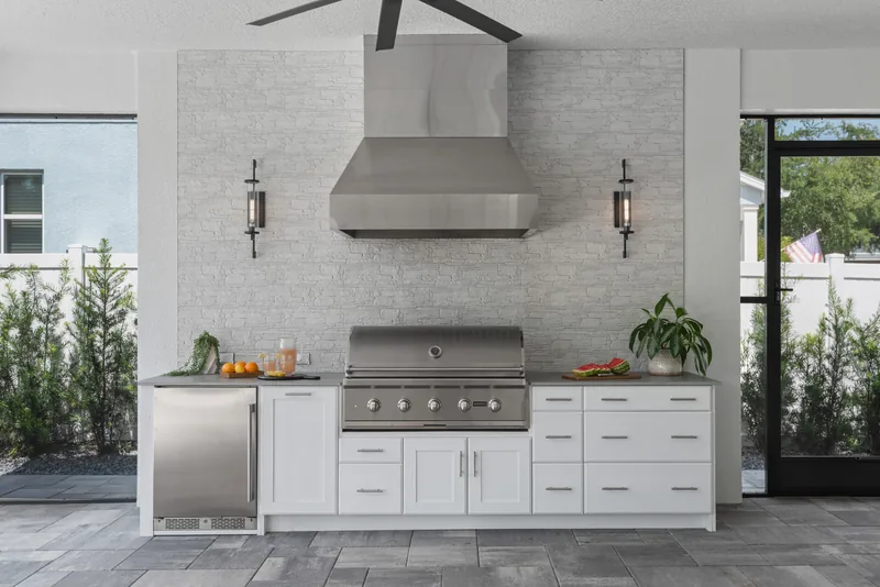 Summer kitchen inside the addition &mdash; stacked-stone feature wall, stainless hood, built-in grill, and weatherproof cabinetry