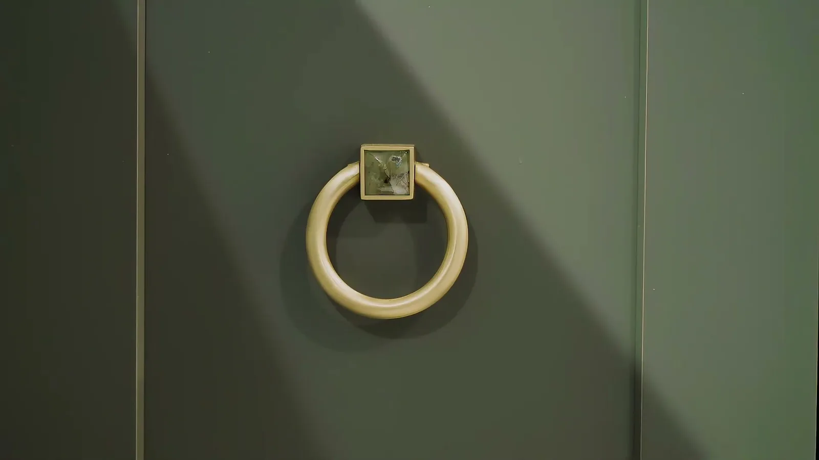 A bronze ring-pull with a marbled inset, centred on a deep-green cabinet door in raking light