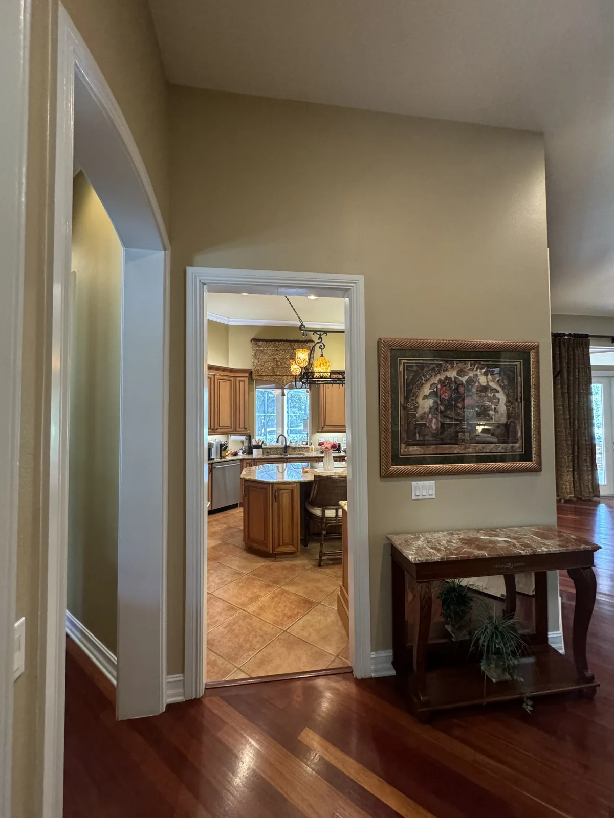 The Winter Springs kitchen before remodeling, seen from the hallway through a cased opening: glazed maple cabinets and an island under a pot-rack chandelier in the distance