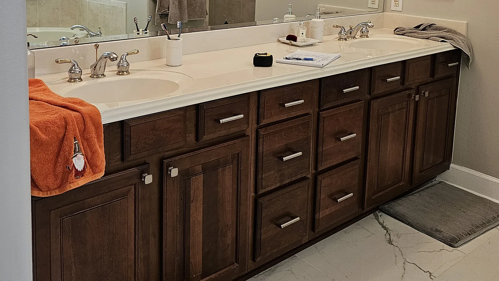 The Winter Park primary bath before remodeling: a cultured-marble double vanity below a full-wall plate mirror, photographed along the same wall