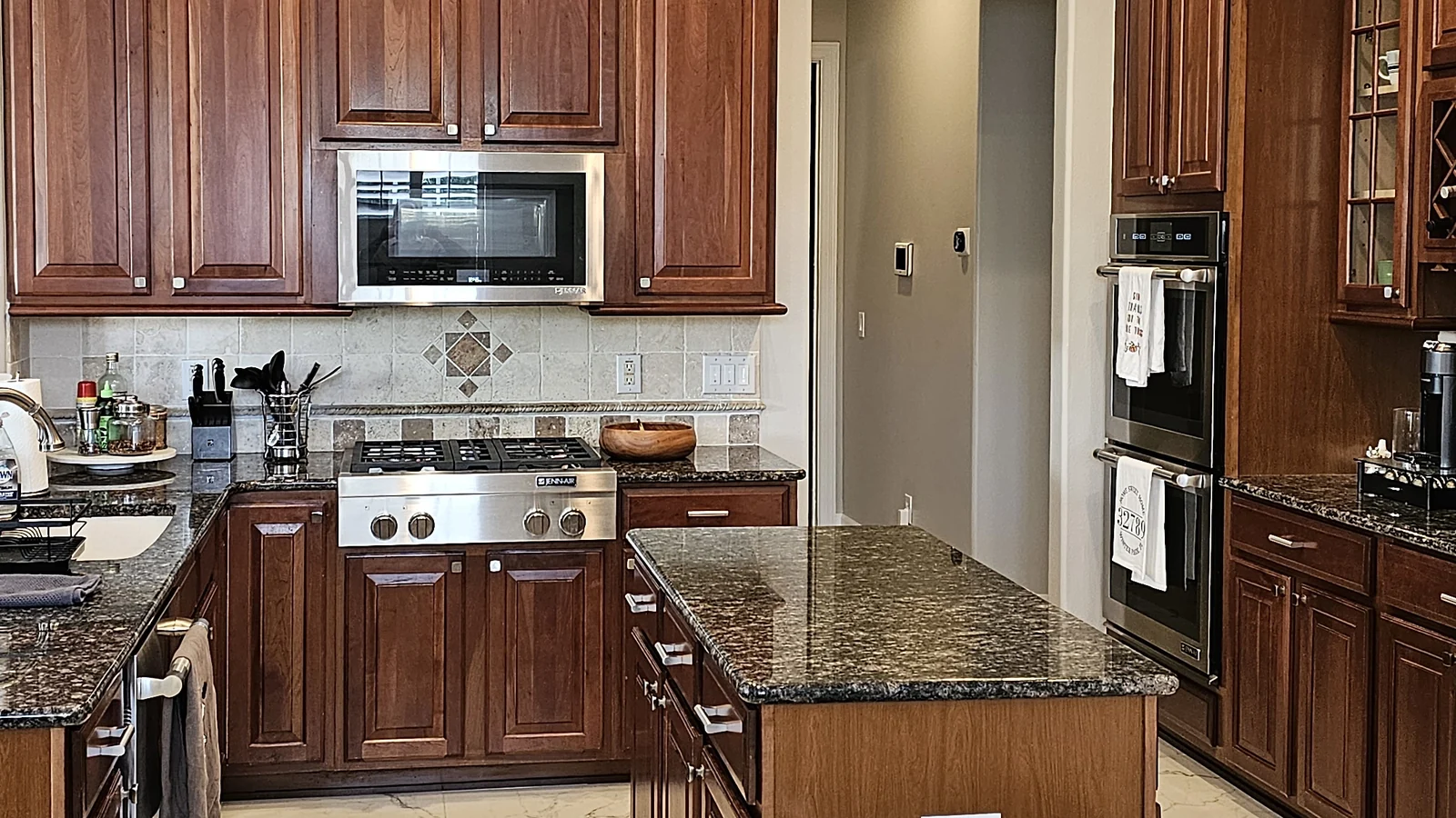 The Winter Park kitchen before remodeling: cherry raised-panel cabinets, brown granite counters, a gas cooktop with microwave above, a small island, and black double wall ovens